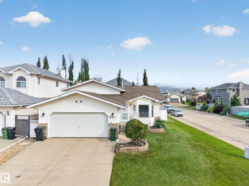 White siding exterior with a two-car garage, concrete driveway, and landscaped front yard with a retaining wall - 365 Hollick-Kenyon Road Nw, Edmonton, AB 