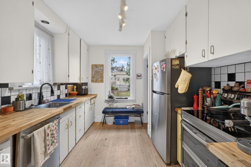 Galley kitchen with wood-finish flooring, white cabinetry, stainless steel appliances, and a checkered backsplash - 11308 123 Street Nw, Edmonton, AB 