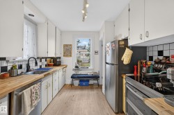 Galley kitchen with wood-finish flooring, white cabinetry, stainless steel appliances, and a checkered backsplash - 