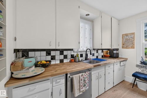 Wood-finish countertops, black and white checkered tile backsplash, white cabinetry, integrated sink, and wood-finish flooring - 11308 123 Street Nw, Edmonton, AB 