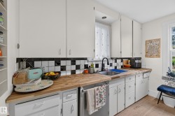 Wood-finish countertops, black and white checkered tile backsplash, white cabinetry, integrated sink, and wood-finish flooring - 