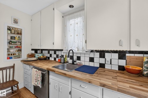 Butcher block countertops, stainless steel sink with a matte black faucet, checkerboard tile backsplash, built-in recessed shelving, and white cabinetry - 11308 123 Street Nw, Edmonton, AB 