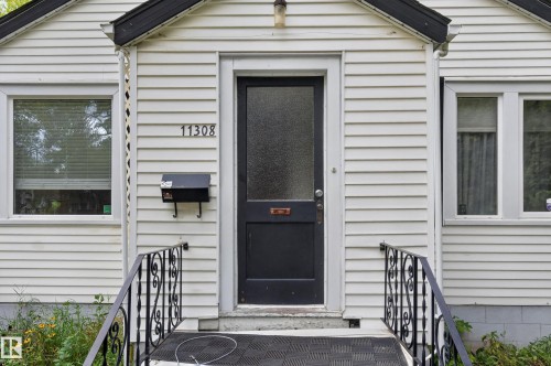 White horizontal siding exterior with a black entry door featuring a frosted glass panel - 11308 123 Street Nw, Edmonton, AB 