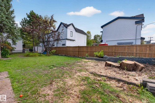 Expansive rear yard featuring a wood fence, mature trees, and a raised garden bed with stone retaining walls - 11308 123 Street Nw, Edmonton, AB 