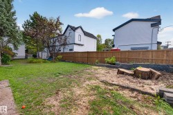 Expansive rear yard featuring a wood fence, mature trees, and a raised garden bed with stone retaining walls - 