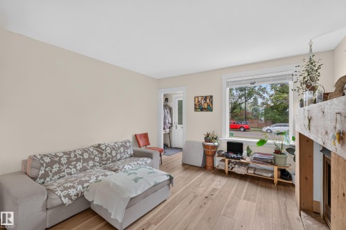 Light-toned walls, wood-finish flooring, a prominent window with white trim, and a rustic wood-clad fireplace surround with a mantel - 11308 123 Street Nw, Edmonton, AB 