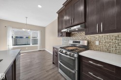 Expansive kitchen featuring dark wood cabinetry, white countertops, stainless steel range with hood, and a decorative tile backsplash - 