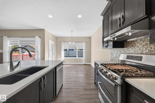 Kitchen featuring a large island with an undermount sink, dark cabinetry, light-toned countertops, and a mosaic tile backsplash - 121 64 Street Sw, Edmonton, AB 