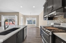 Kitchen featuring a large island with an undermount sink, dark cabinetry, light-toned countertops, and a mosaic tile backsplash - 