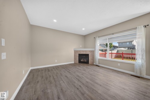 Spacious room featuring wood-finish flooring, a contemporary fireplace with a tiled surround, a wide window, and recessed lighting - 121 64 Street Sw, Edmonton, AB 