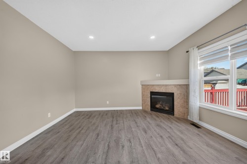Recessed lighting, wood-finish flooring, corner fireplace with a tiled surround, and a large window with privacy blinds - 121 64 Street Sw, Edmonton, AB 