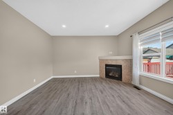 Recessed lighting, wood-finish flooring, corner fireplace with a tiled surround, and a large window with privacy blinds - 