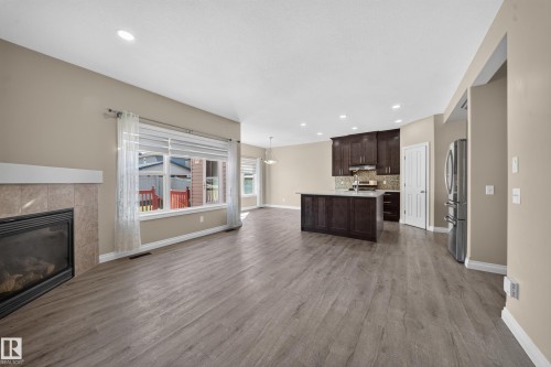 Tile-surround fireplace, wood-finish flooring, recessed lighting, kitchen island with sink, and stainless steel appliances - 121 64 Street Sw, Edmonton, AB 