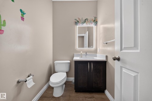 Powder room featuring a dark wood-finish vanity, white countertop with an integrated sink, and an illuminated mirror - 121 64 Street Sw, Edmonton, AB 