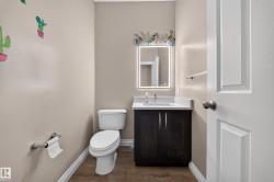 Powder room featuring a dark wood-finish vanity, white countertop with an integrated sink, and an illuminated mirror - 
