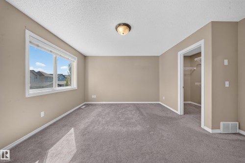 Wall-to-wall carpeting, neutral wall finishes, window with white trim, and a built-in closet with shelving - 121 64 Street Sw, Edmonton, AB 