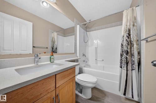 Bathroom featuring a wood-finish vanity with an integrated rectangular sink, light-toned countertop, and a shower-tub combination with white paneling - 121 64 Street Sw, Edmonton, AB 
