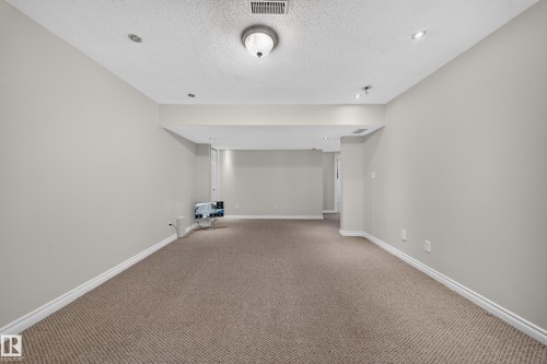 Spacious room featuring neutral carpeting, light gray wall paint, recessed lighting, and a drop ceiling with a central flush mount light fixture - 121 64 Street Sw, Edmonton, AB 