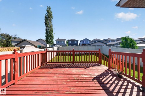 Expansive wood deck with red railings and stairs, overlooking a fenced backyard with a manicured lawn - 121 64 Street Sw, Edmonton, AB 
