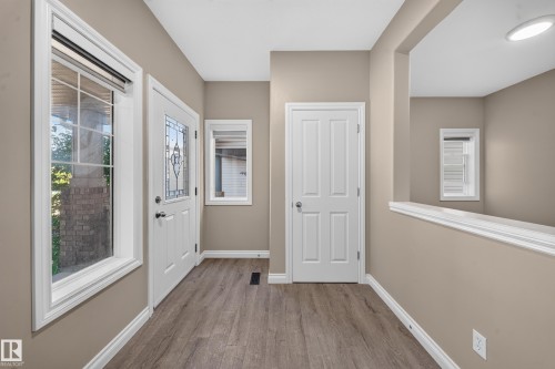 Entryway featuring wood-finish flooring, a white paneled door, a door with decorative glass, and a large window with grid panes - 121 64 Street Sw, Edmonton, AB 