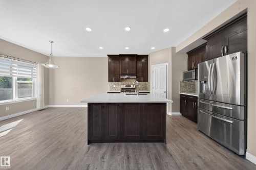 Open-concept kitchen featuring dark wood cabinetry, stainless steel appliances, a center island with a light-colored countertop, and recessed lighting - 121 64 Street Sw, Edmonton, AB 