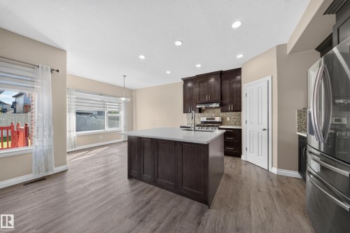 Kitchen featuring a central island with white countertop, dark wood-finish cabinetry, stainless steel appliances, and a tiled backsplash - 121 64 Street Sw, Edmonton, AB 