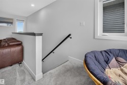 Carpeted staircase with a modern black handrail, framed by light gray walls - 