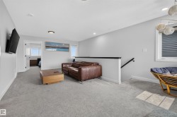 Carpeted secondary living space with a white half-wall and black handrail, featuring recessed lighting, a modern flush-mount light fixture, and two windows - 