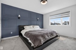 Bedroom featuring a decorative accent wall with panel molding, light gray carpet, and a window with blinds - 