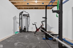 Unfinished basement space featuring exposed ceiling joists, light-colored walls, and dark-toned flooring - 
