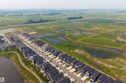 Aerial perspective showcasing a developed residential street with modern homes, a tranquil pond, and an adjacent paved pathway - 
