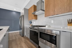 Well-appointed kitchen featuring stainless steel appliances, wood-finish upper cabinetry, light gray lower cabinetry, and light quartz countertops - 