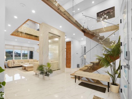High-gloss tile flooring, custom interior water feature, open-tread staircase with glass railing, recessed ceiling lighting, and large windows with roller blinds - 4809 Woolsey Lane Nw, Edmonton, AB 