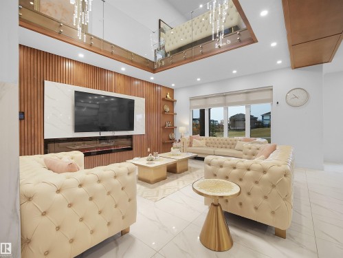 High ceilings with recessed lighting, large windows with roller shades, white tile flooring, wood-paneled accent wall with built-in shelving, and a linear electric fireplace - 4809 Woolsey Lane Nw, Edmonton, AB 