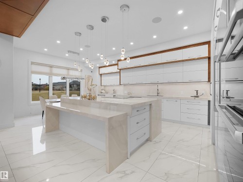 Spacious kitchen featuring an extended waterfall island, white cabinetry with wood-finish accents, integrated stainless steel appliances, and large format porcelain tile flooring - 4809 Woolsey Lane Nw, Edmonton, AB 