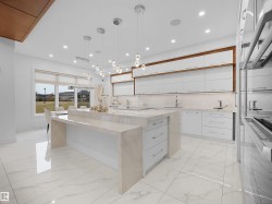 Spacious kitchen featuring an extended waterfall island, white cabinetry with wood-finish accents, integrated stainless steel appliances, and large format porcelain tile flooring - 