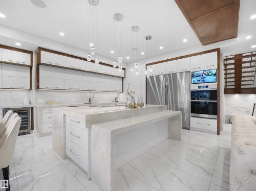 Modern kitchen featuring a large waterfall island, white cabinetry with wood-finish framing, stainless steel appliances, and recessed lighting - 4809 Woolsey Lane Nw, Edmonton, AB 