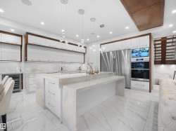 Modern kitchen featuring a large waterfall island, white cabinetry with wood-finish framing, stainless steel appliances, and recessed lighting - 