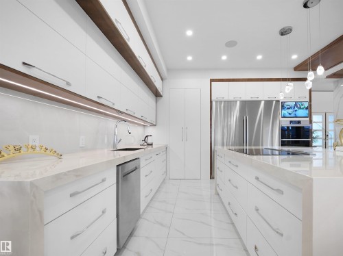 Contemporary kitchen featuring white cabinetry with integrated wood-finish accents, expansive countertops, recessed lighting, and stainless steel appliances - 4809 Woolsey Lane Nw, Edmonton, AB 