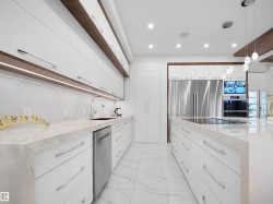 Contemporary kitchen featuring white cabinetry with integrated wood-finish accents, expansive countertops, recessed lighting, and stainless steel appliances - 
