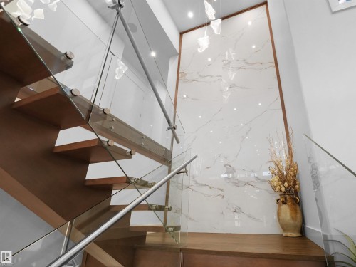 Open-riser staircase featuring wood treads and glass railings with stainless steel accents - 4809 Woolsey Lane Nw, Edmonton, AB 
