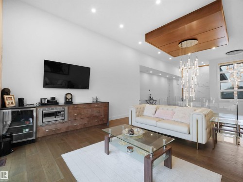 Recessed lighting illuminates the wood-finish flooring, complemented by a built-in media console with integrated refrigeration - 4809 Woolsey Lane Nw, Edmonton, AB 