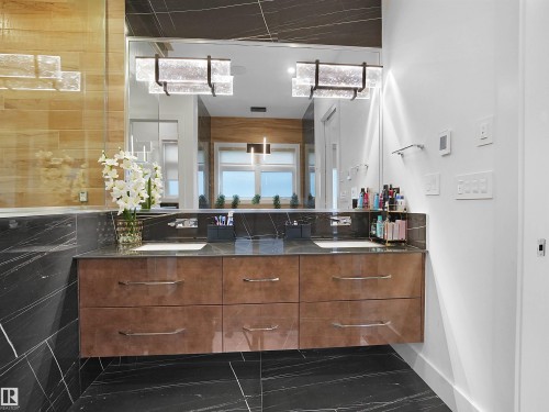Dual vanity with a floating wood-finish cabinet, integrated sinks, dark stone countertops, and full-wall mirror - 4809 Woolsey Lane Nw, Edmonton, AB 