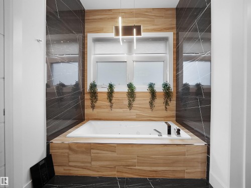 Built-in soaking tub with a tiled surround, framed window, dark tile accent walls, and recessed lighting - 4809 Woolsey Lane Nw, Edmonton, AB 
