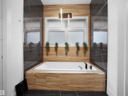 Built-in soaking tub with a tiled surround, framed window, dark tile accent walls, and recessed lighting - 