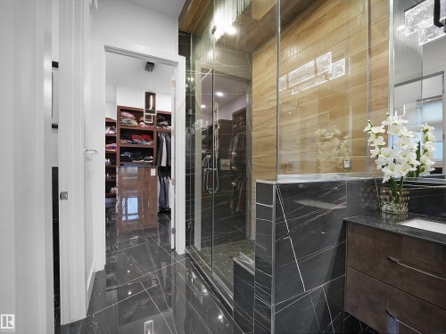 Polished dark tile flooring, glass-enclosed shower, dark wood-finish vanity, built-in shelving, and light wood-finish wall tile - 4809 Woolsey Lane Nw, Edmonton, AB 