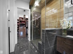 Polished dark tile flooring, glass-enclosed shower, dark wood-finish vanity, built-in shelving, and light wood-finish wall tile - 