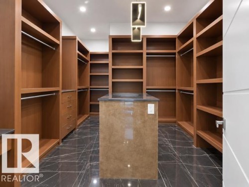Custom walk-in closet featuring extensive built-in shelving, integrated drawers, and a central island with a solid surface countertop - 4809 Woolsey Lane Nw, Edmonton, AB 