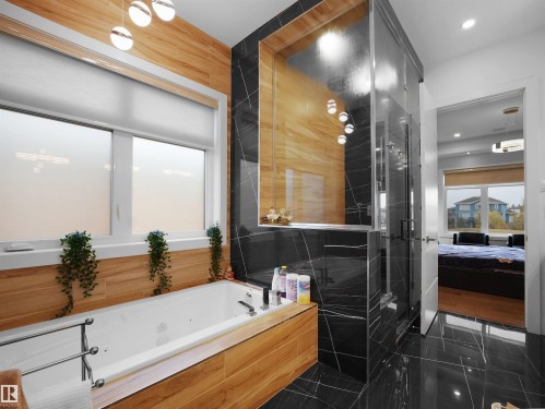 Jetted soaking tub with wood-finish paneling, glass-enclosed shower with black marble-style tile, and contemporary overhead lighting - 4809 Woolsey Lane Nw, Edmonton, AB 