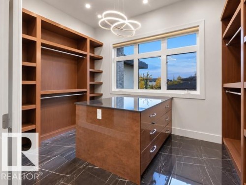 Built-in shelving and hanging rods, central island with drawers and a dark countertop, large multi-pane window, modern overhead light fixture, and dark tile flooring - 4809 Woolsey Lane Nw, Edmonton, AB 